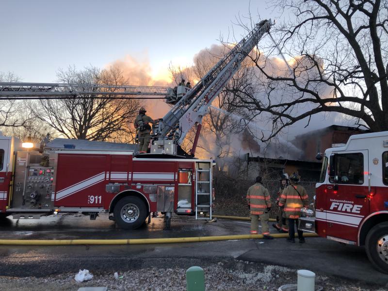 Members of the Independence Fire Department utilize a latter truck and pumper truck to fight a residential fire with smoke coming out of the roof.