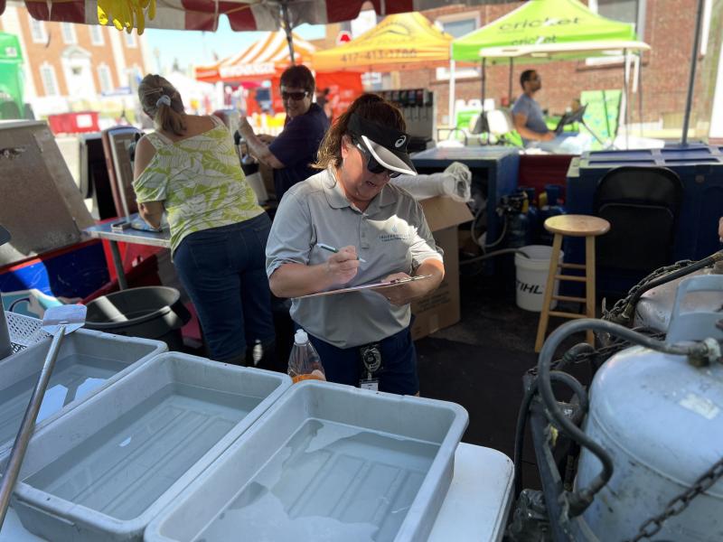 An Independence Health Inspector reviews the checklist for a vendor at the SantaCaliGon Festival next to a hand cleaning station. 
