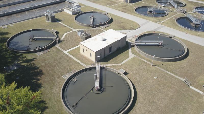 Image taken facing southeasterly. Four round, 60-foot diameter basins holding liquid. A white building sits in the center of the pools. Walkways are seen stretching out to the center of each pool.