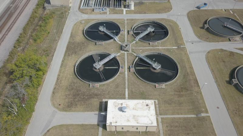 Image taken northeasterly. Four round, 60-foot diameter basins holding liquid. A white building sits off center of the pools. Walkways are seen stretching out to the center of each pool, meeting in the middle at a singular metal platform..